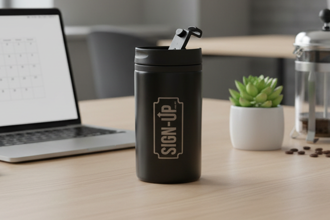 Black travel mug with custom logo branding on a desk with laptop, coffee press, and cup.