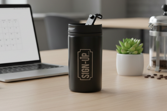 Black travel mug with custom logo branding on a desk with laptop, coffee press, and cup.